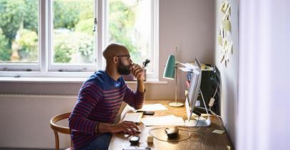 a person working from home sitting at a desk looking at a computer screen