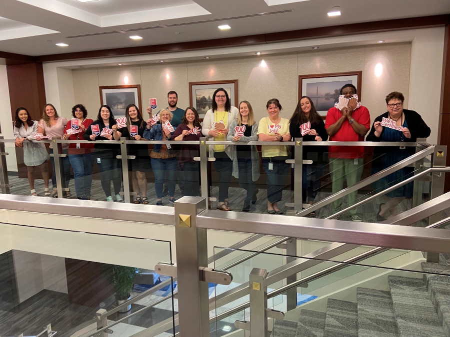 A group of LGRA employees celebrating with fun signs and balloons Great Place to work award standing in a line overlooking the staircase